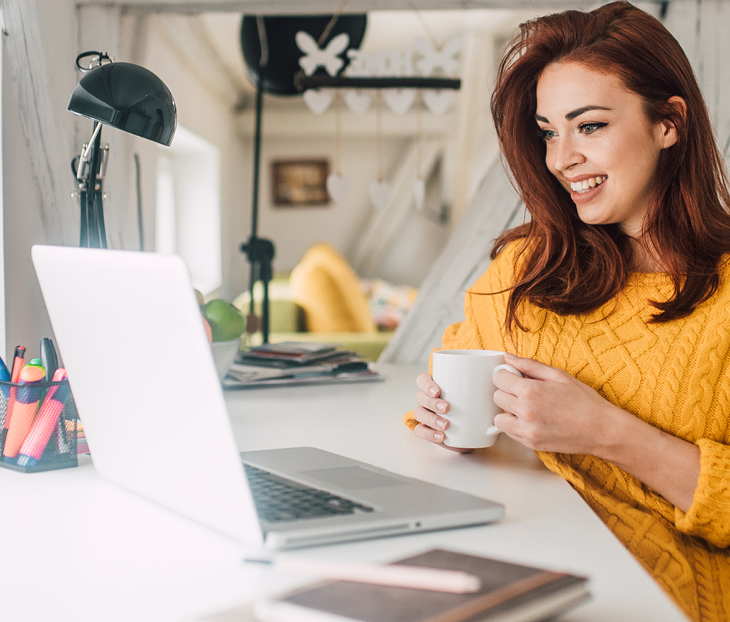 Women searching for online learning courses while using a laptop and sitting at a desk holding a mug.